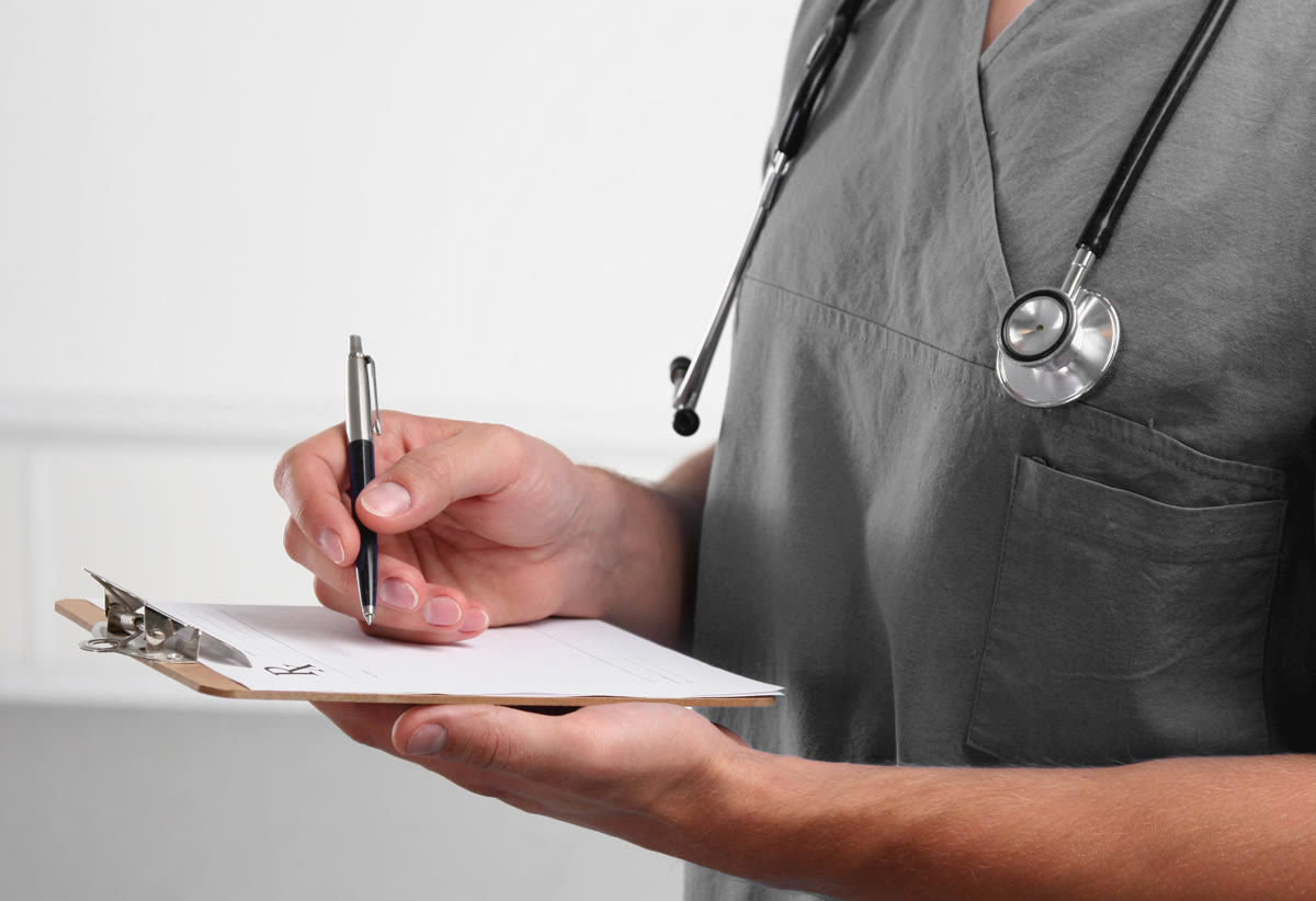 Médico con estetoscopio anotando los hallazgos del examen físico en su tabla