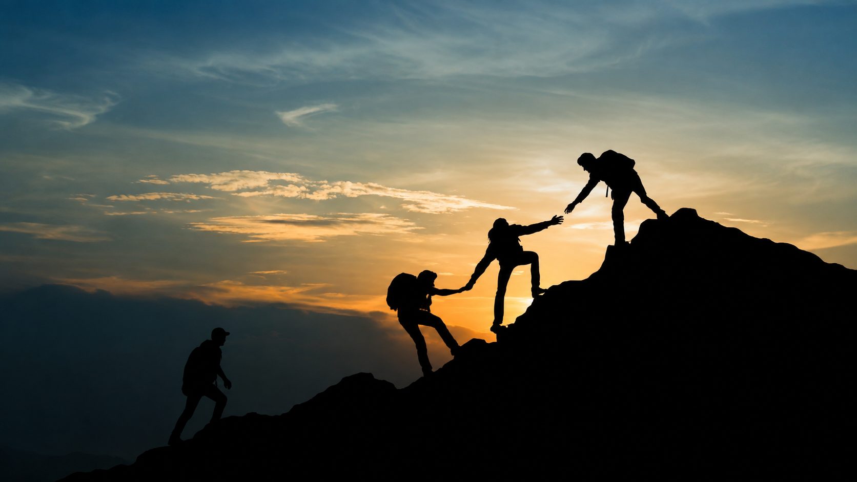 Excursionistas ayudándose a subir a la cima de una montaña al atardecer